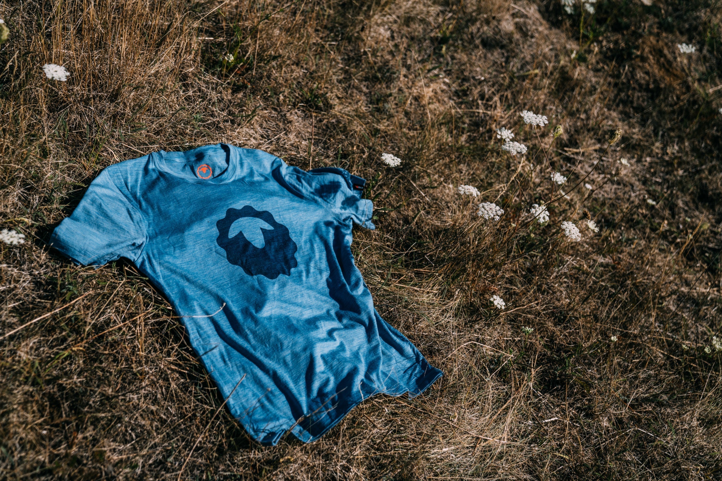 A blue Isobaa merino t-shirt laid on dry summer grass