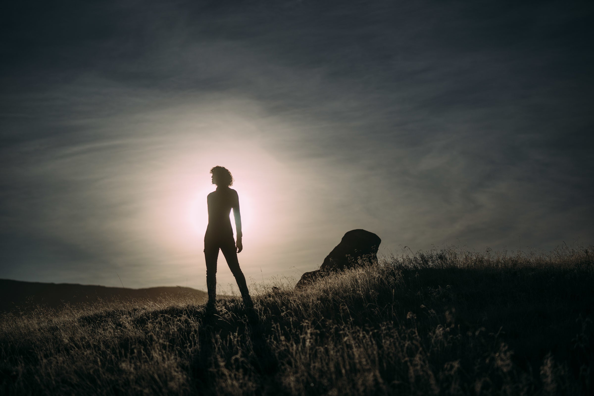 Eine Silhouette einer Person auf einem Hügel, von der untergehenden Sonne hinterleuchtet vor klarem Himmel.