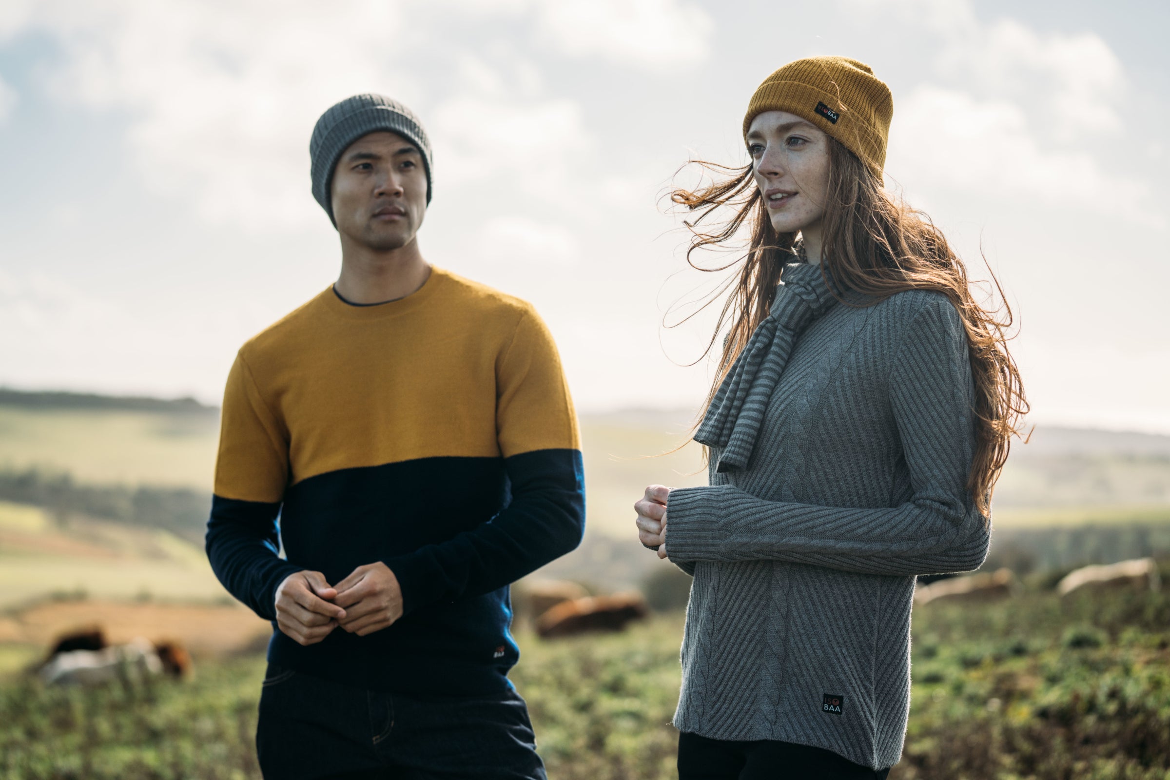 Two people wearing colorful sweaters and beanies standing in a field
