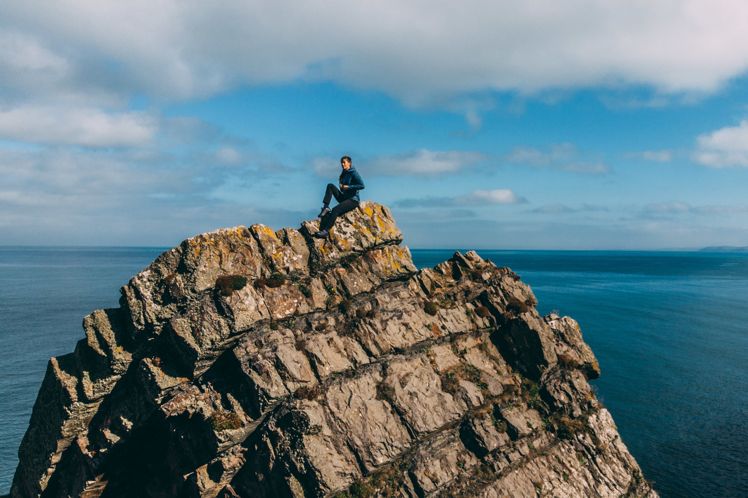 Eine Person sitzt auf einer felsigen Klippe mit Blick auf das Meer